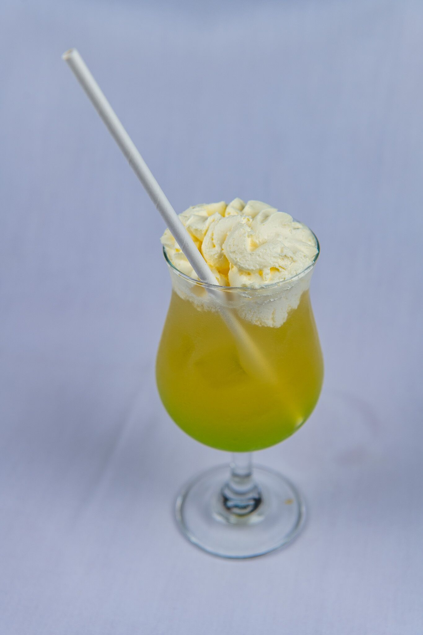 Un vaso de cóctel con una pajita, lleno de un líquido amarillo y coronado con una bola de helado.