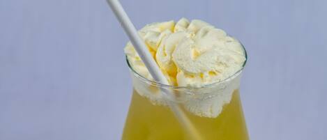 Un vaso de cóctel con una pajita, lleno de un líquido amarillo y coronado con una bola de helado.