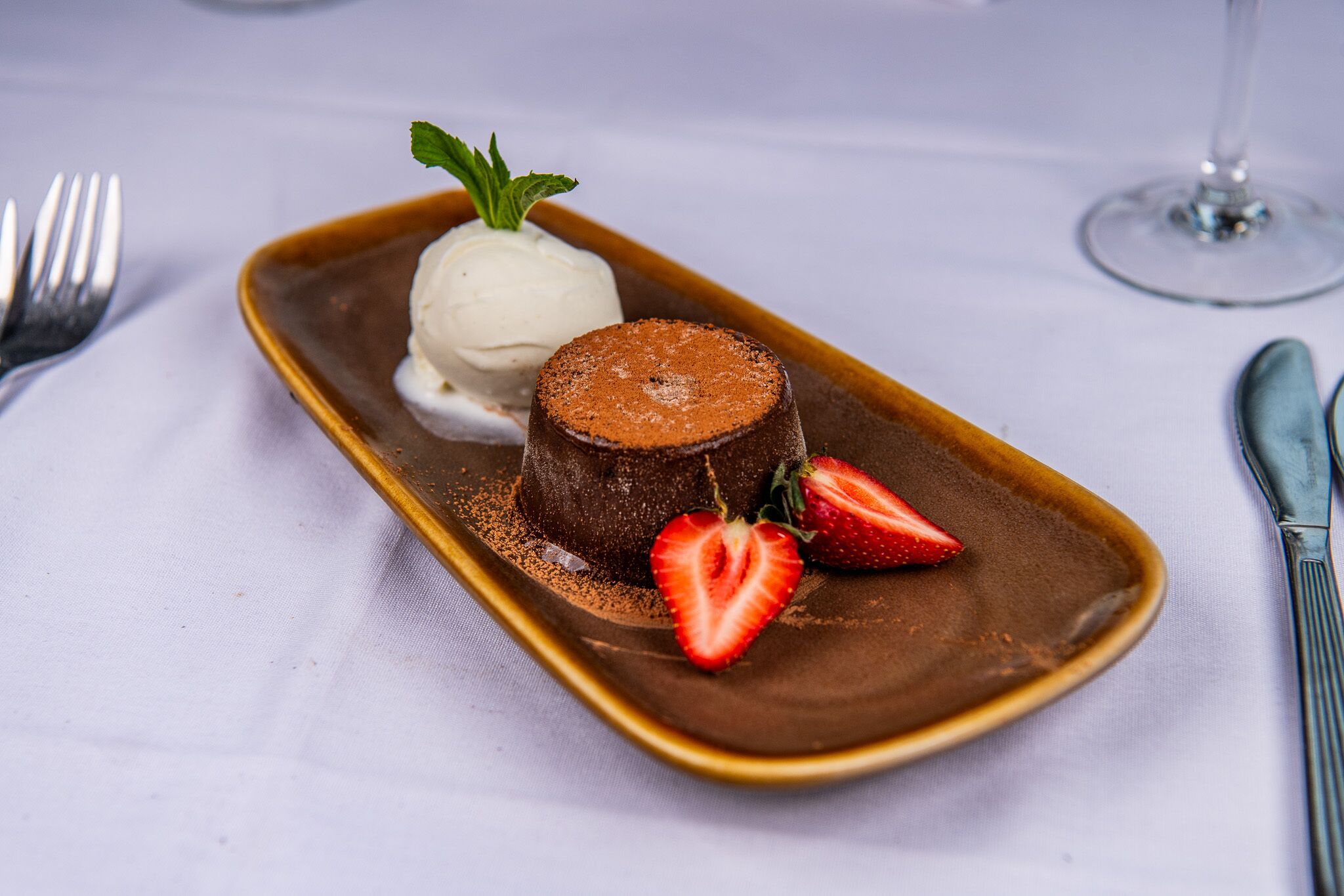 Un plat de postres amb un pastís de lava de xocolata, una bola de gelat de vainilla i maduixes.