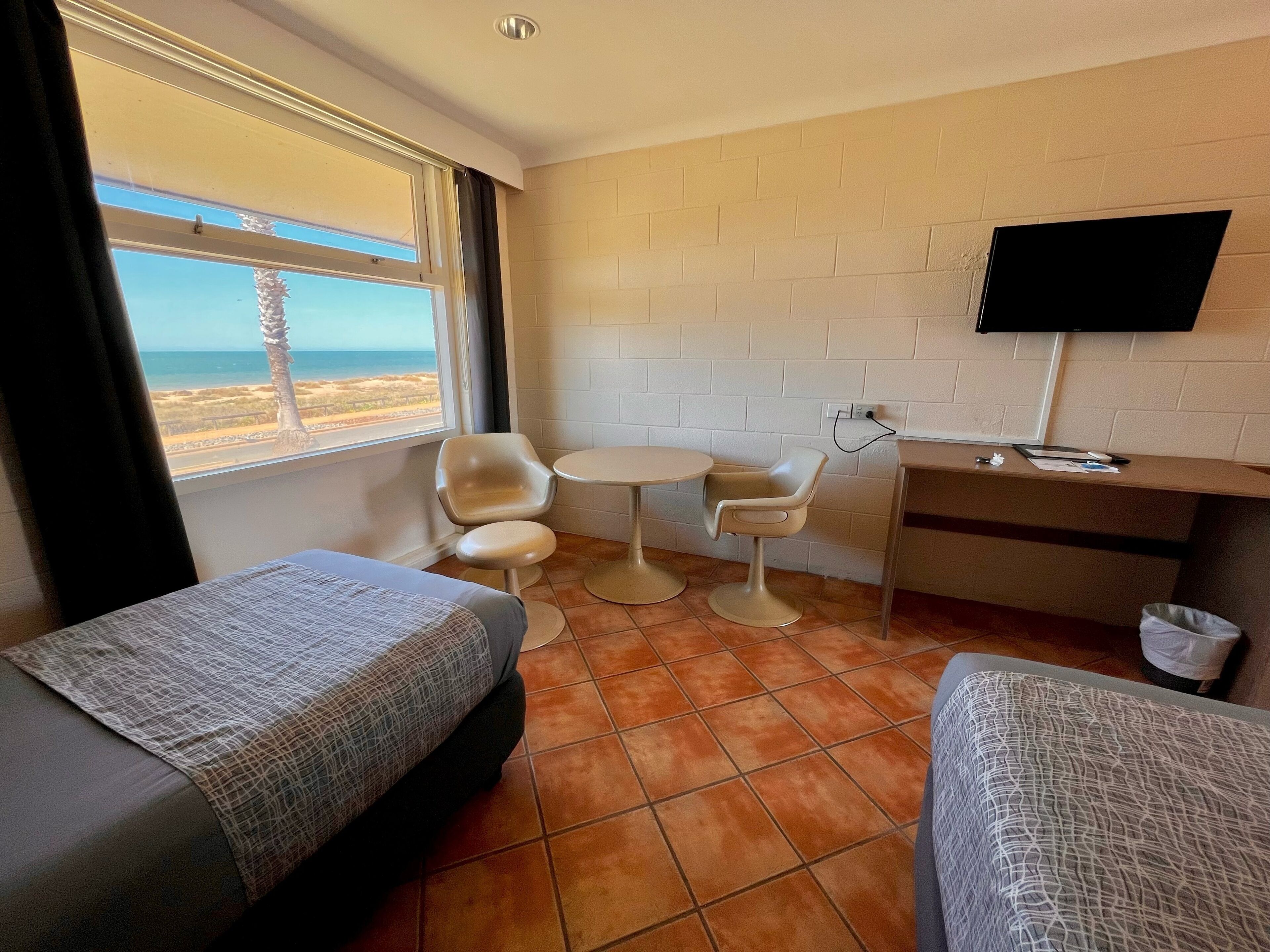 Habitación de hotel con dos camas, una mesita, televisor y vista a la playa.