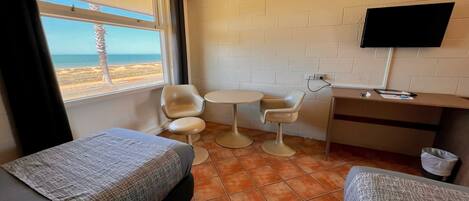 Habitación de hotel con dos camas, una mesita, televisor y vista a la playa.