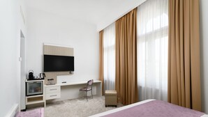 Una habitación de hotel con cama, escritorio, silla, televisor y ventana con cortinas.