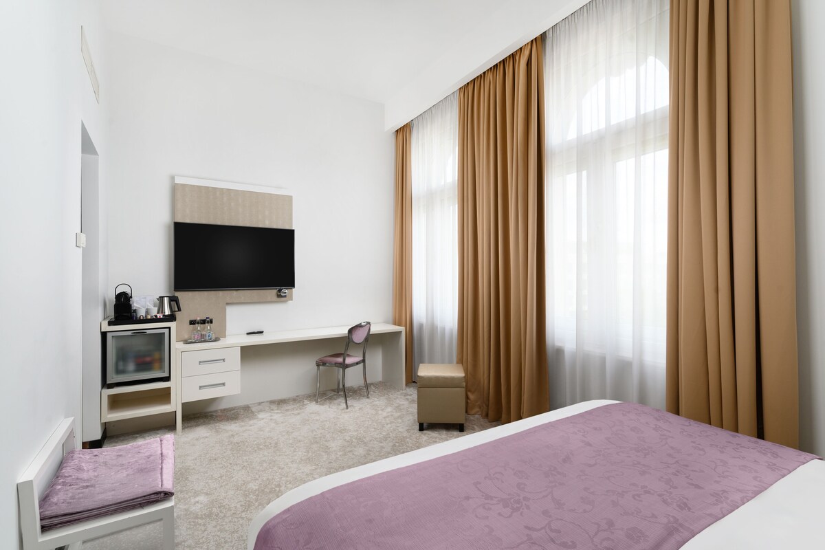 A hotel room with a bed, a desk, a chair, a television, and a window with curtains.