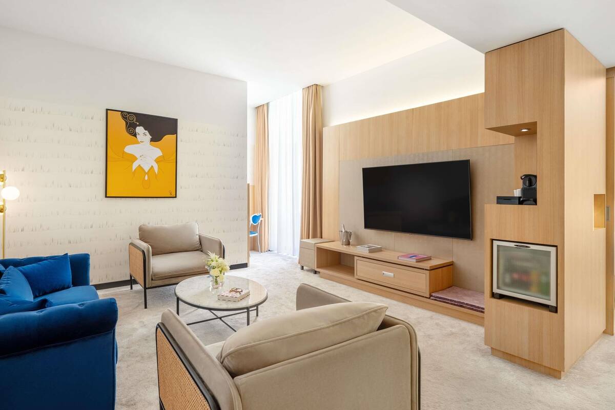 A modern living room with a sofa, armchair, coffee table, and a flat-screen TV mounted on a wooden wall.