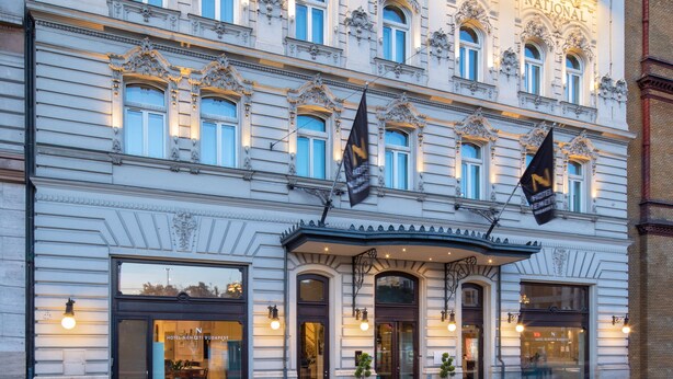 Un edificio histórico con detalles arquitectónicos ornamentales, múltiples ventanas y banderas.