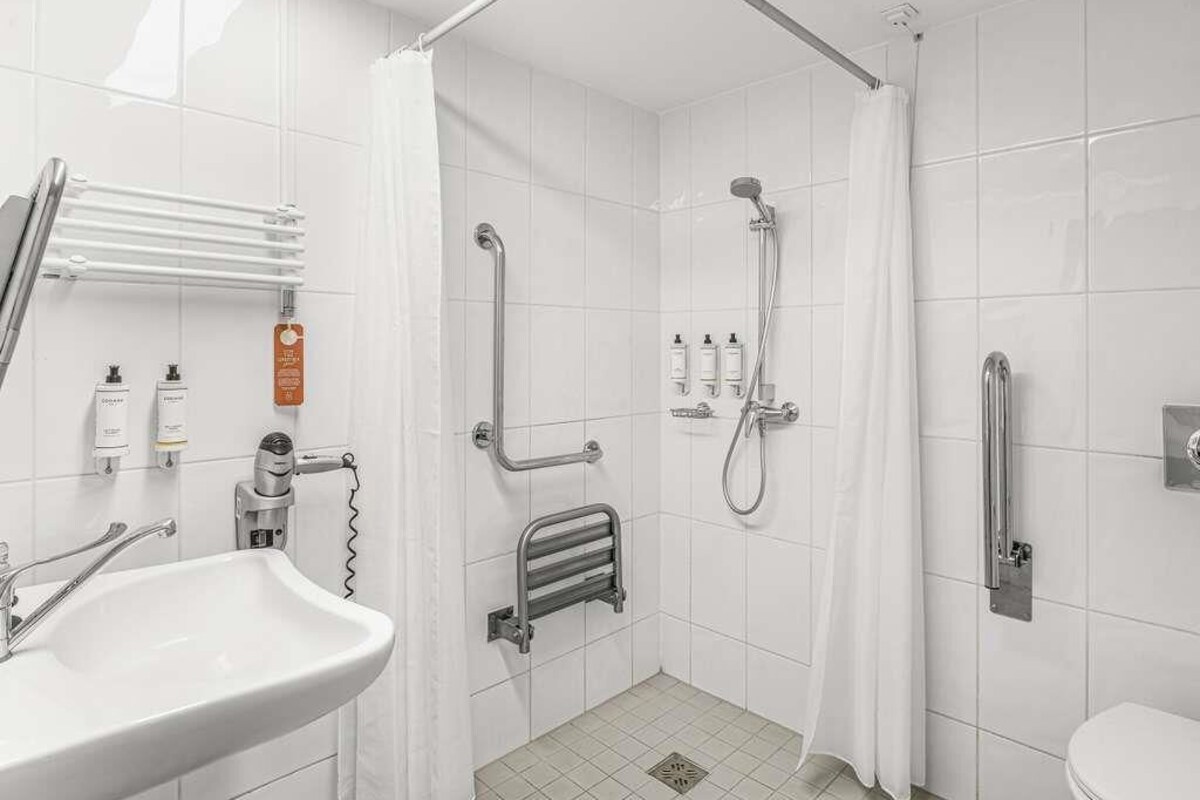 A bathroom with a shower, toilet, and sink, equipped with grab bars and a towel rack.