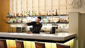 A bar area with a bartender, shelves of liquor bottles, and bar stools.