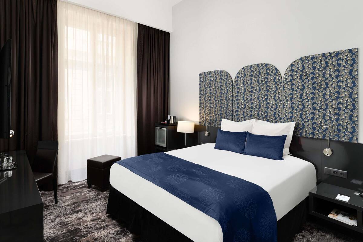 A hotel room with a large bed, a desk, a chair, and a TV.