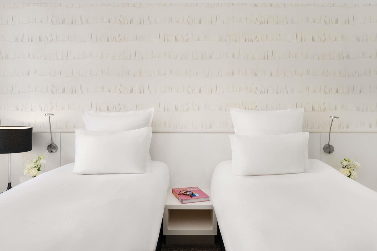 Une chambre d’hôtel avec deux lits, une table de chevet, une lampe et un mur orné d’un motif texturé.