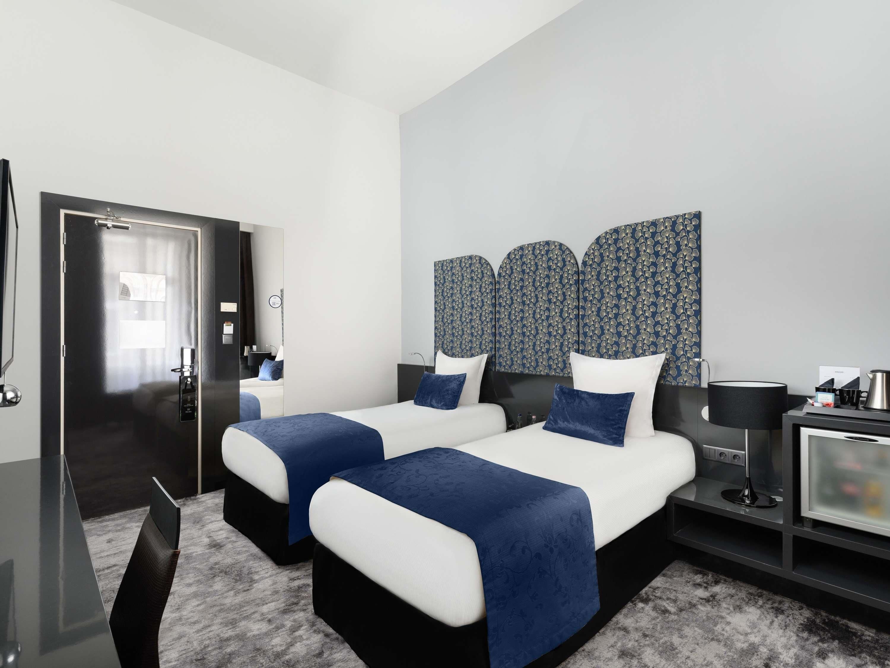 A hotel room with two beds, a desk, a TV, and a mirror.
