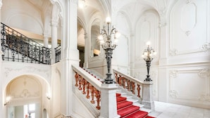 A grand staircase with red carpet, ornate railings, and a chandelier.