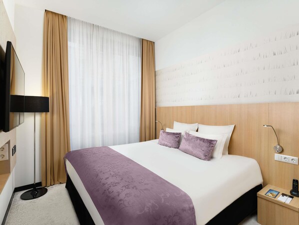 A hotel room with a bed, a TV, a bedside table, and a wall-mounted light. - Nemzeti Hotel Budapest - MGallery Collection (Budapest)