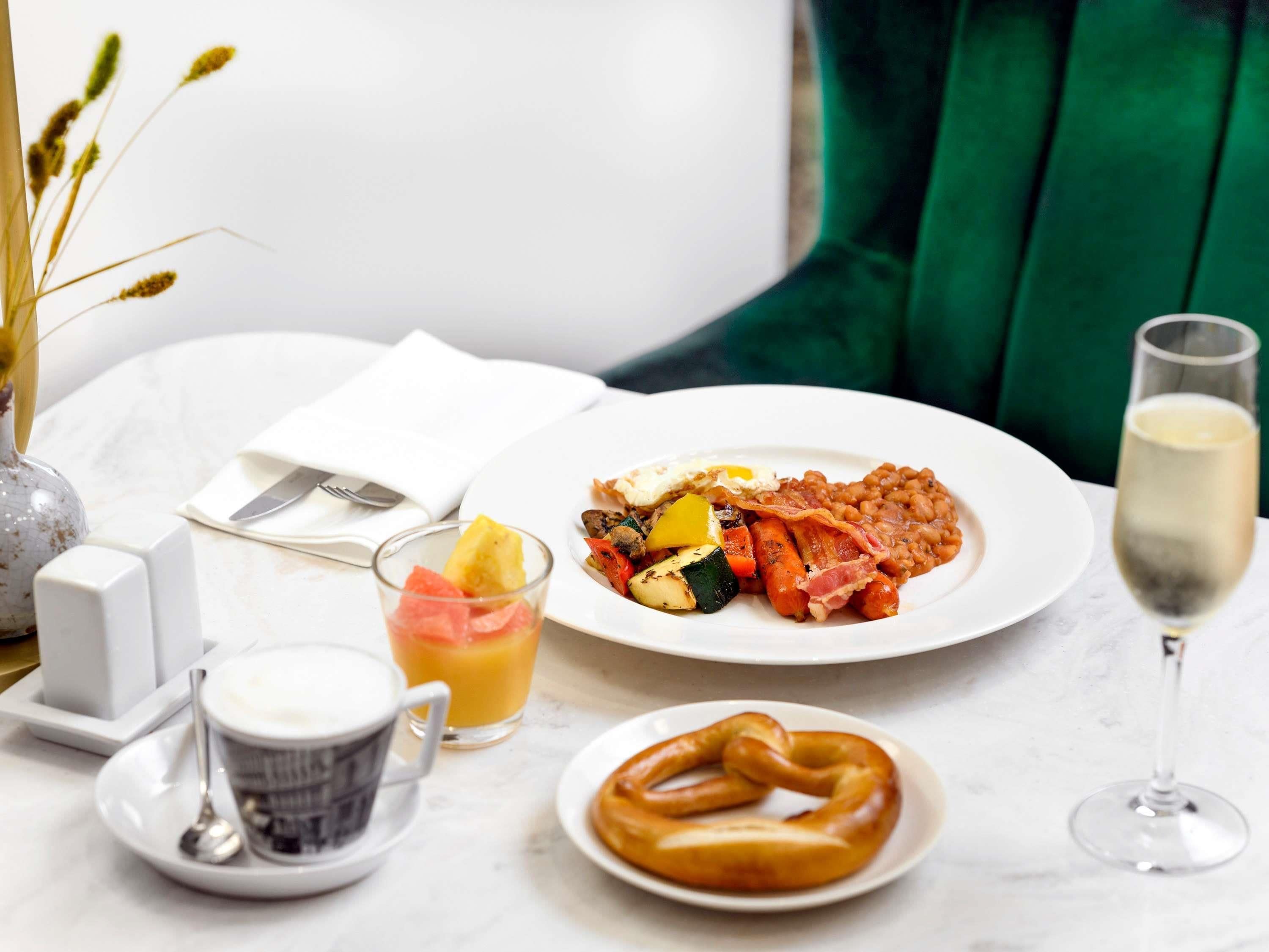A breakfast setting with a plate of food, a glass of juice, a cup of coffee, a pretzel, and a glass of wine.