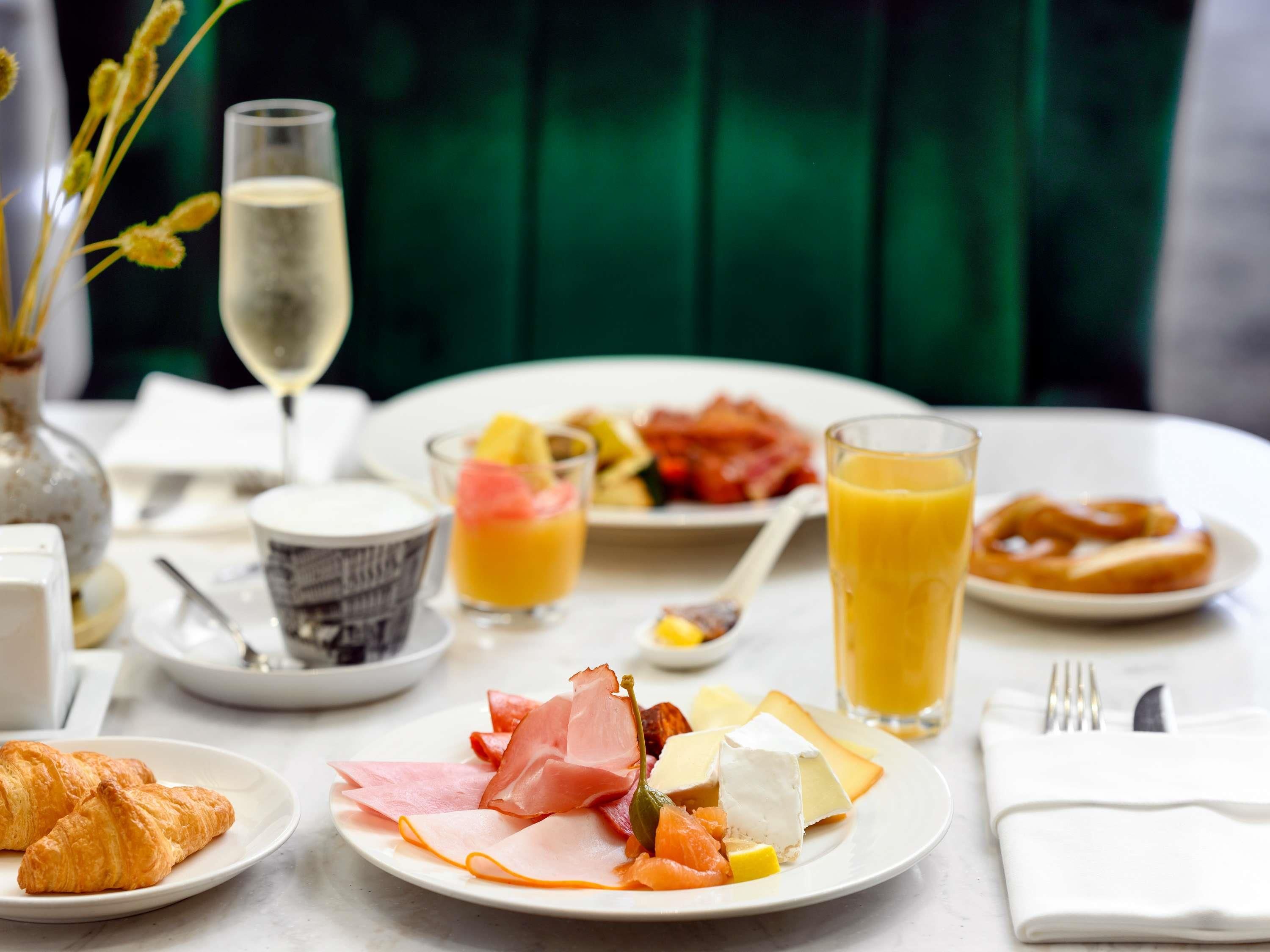 Un desayuno con cruasanes, jamón, queso, frutas y jugo sobre una mesa.