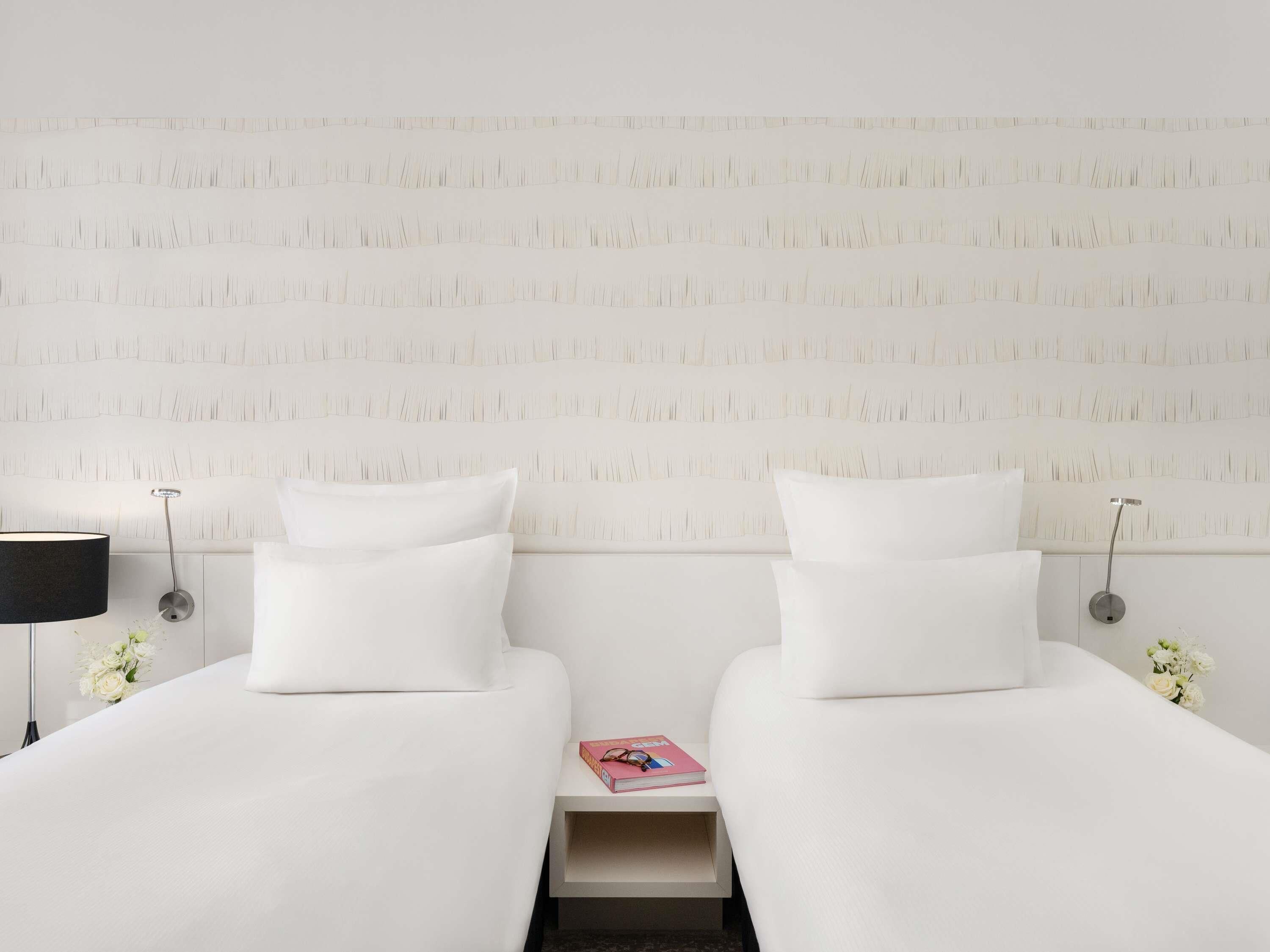 Une chambre d’hôtel avec deux lits, une table de chevet, une lampe et un luminaire fixé au mur.