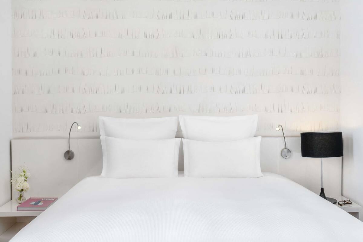 A neatly made bed with white linens, a bedside table with a lamp, and a wall with a textured pattern.