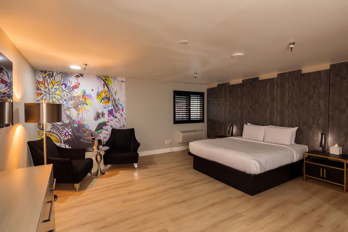 A modern bedroom with a large bed, a desk, a chair, and a colorful mural on the wall.