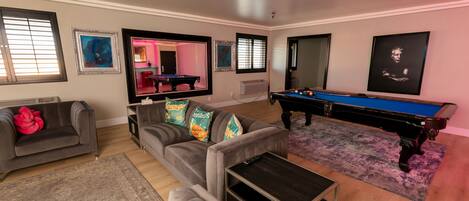 A living room with a pool table, two sofas, a coffee table, and artwork on the walls.
