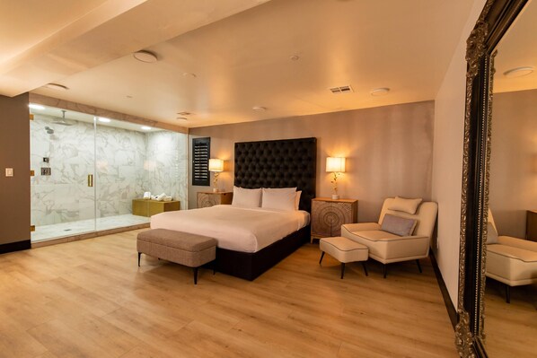A hotel room with a large bed, a seating area with two chairs, a glass shower enclosure, and a large mirror. - The Lexi Las Vegas, Trademark Collection by Wyndham (Las Vegas)