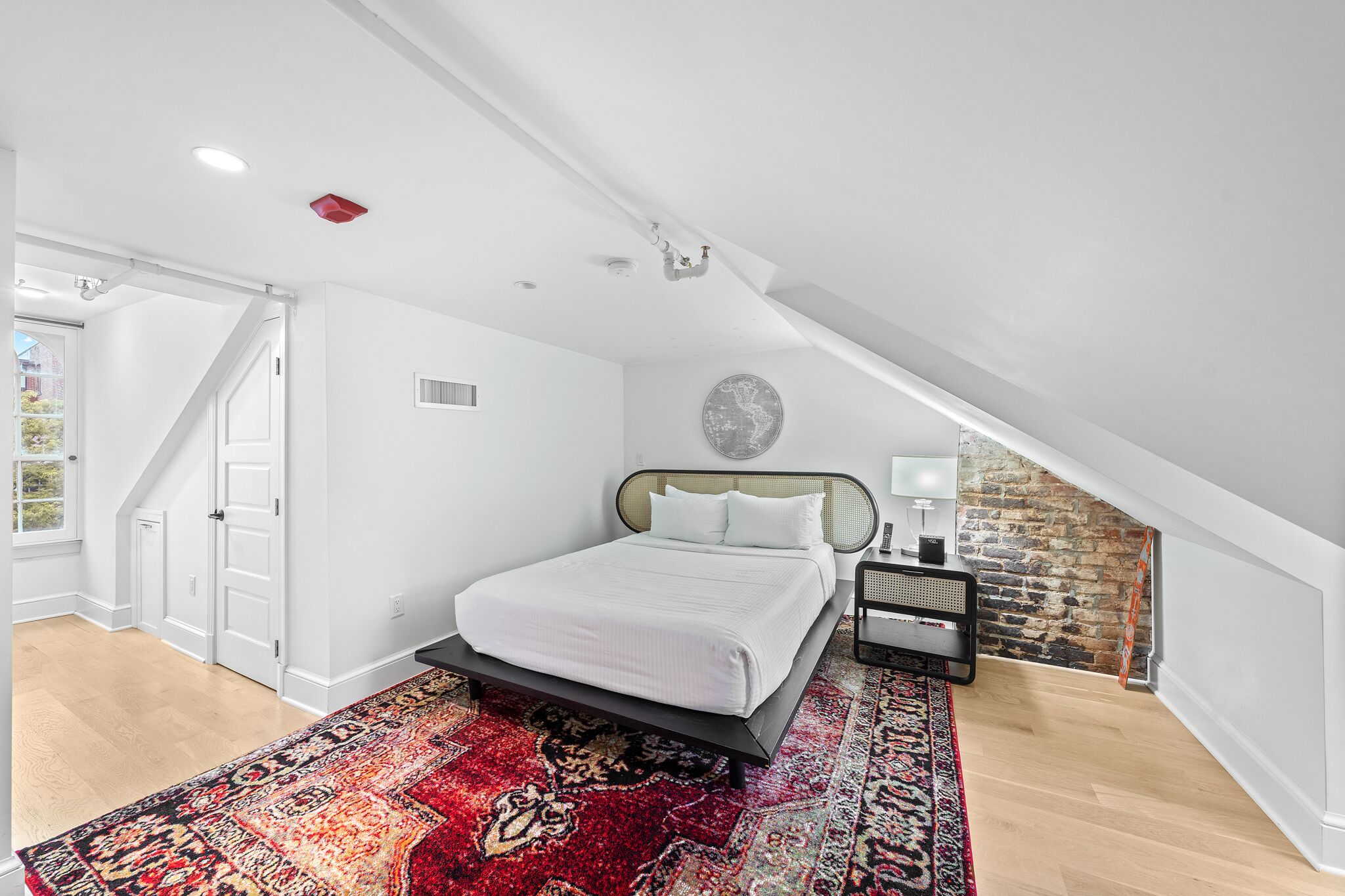 A bedroom with a bed, a patterned rug, a white door, and a brick wall.