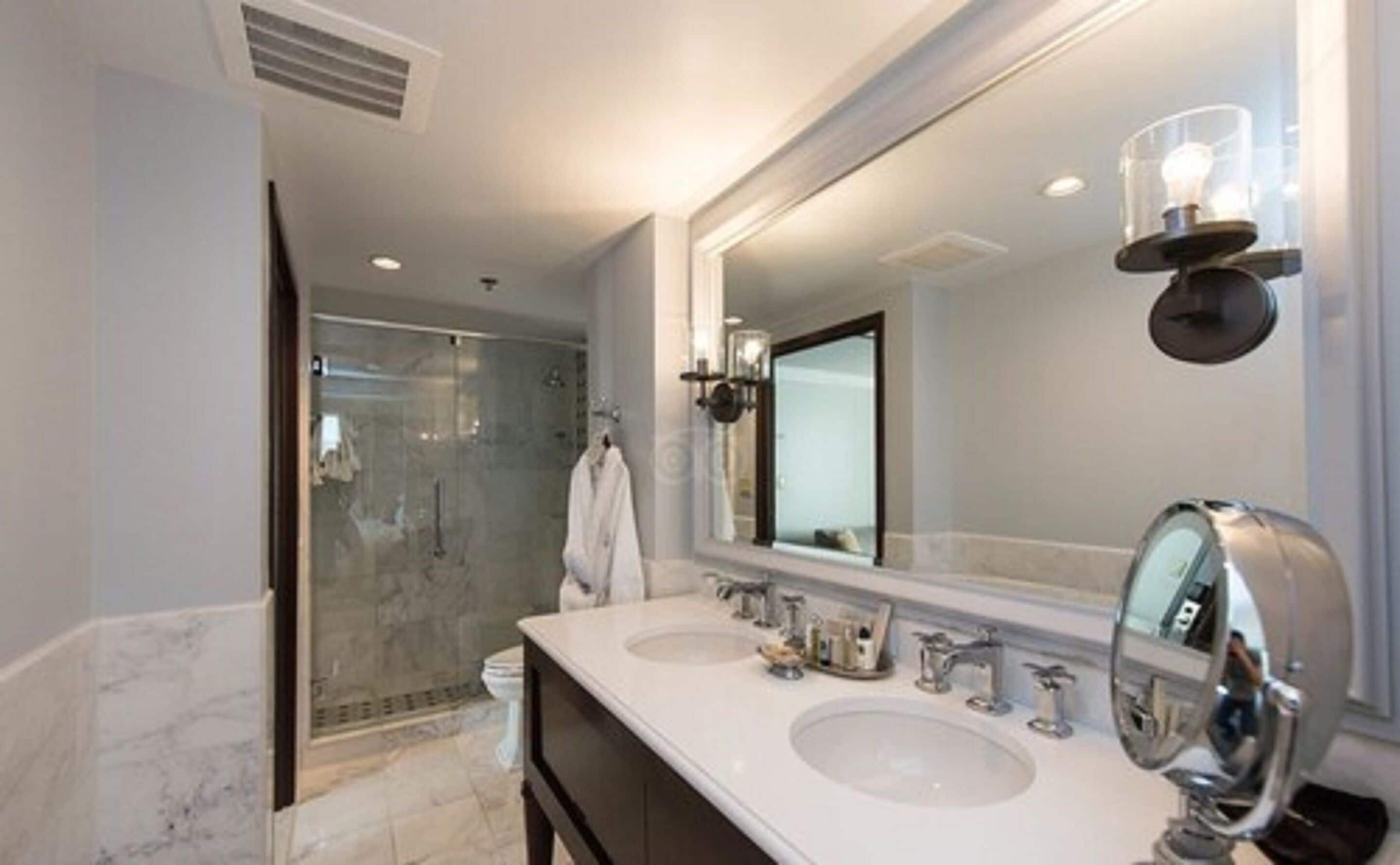 Un baño moderno con dos lavamanos, un espejo grande y una cabina de ducha de vidrio.