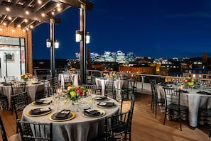 Un área de comedor en la azotea con mesas dispuestas para la cena, con vistas al horizonte de la ciudad.