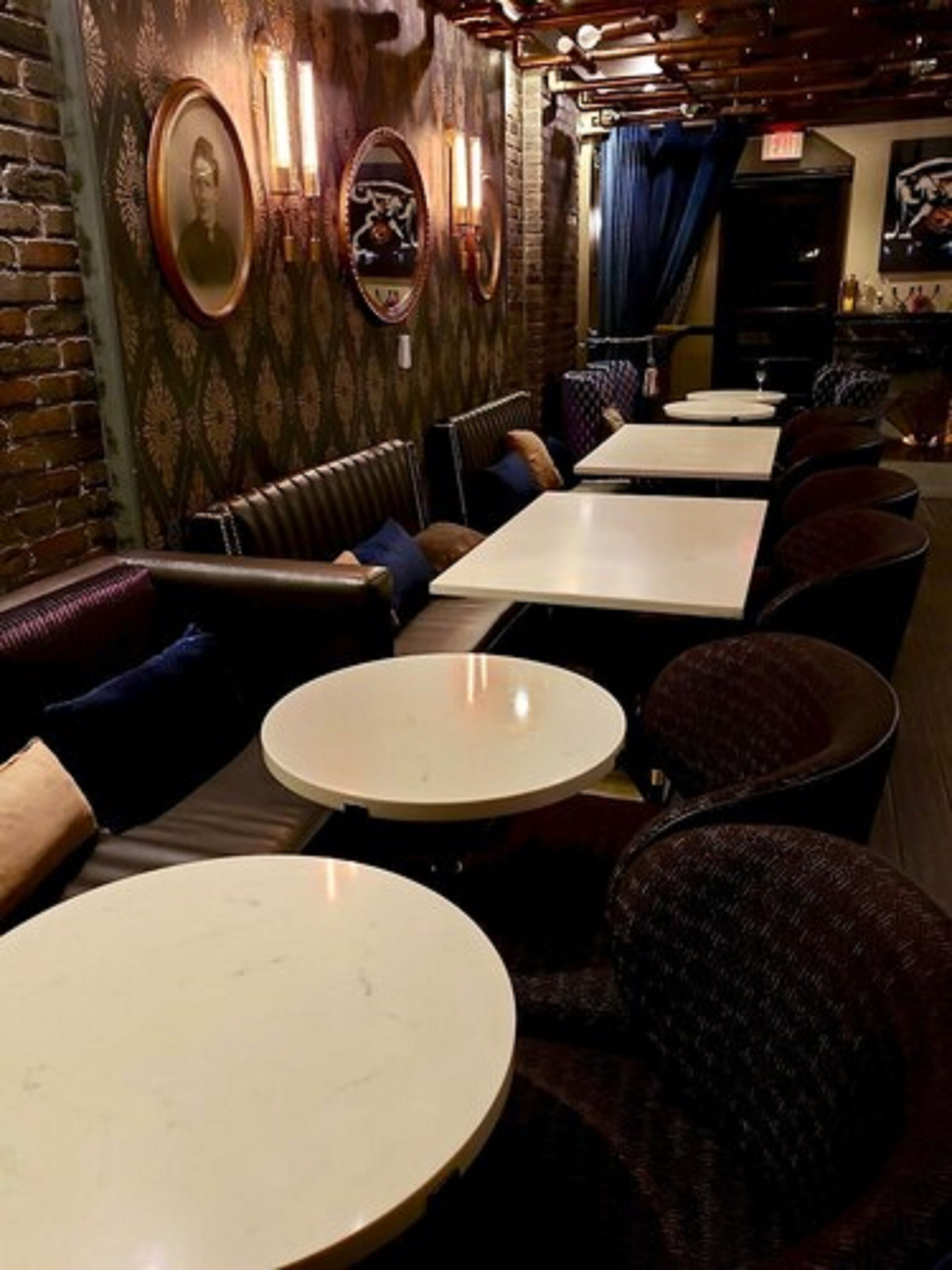 Een restaurantinterieur met bakstenen muren, lijstwerken, lederen zitbanken en ronde tafels.