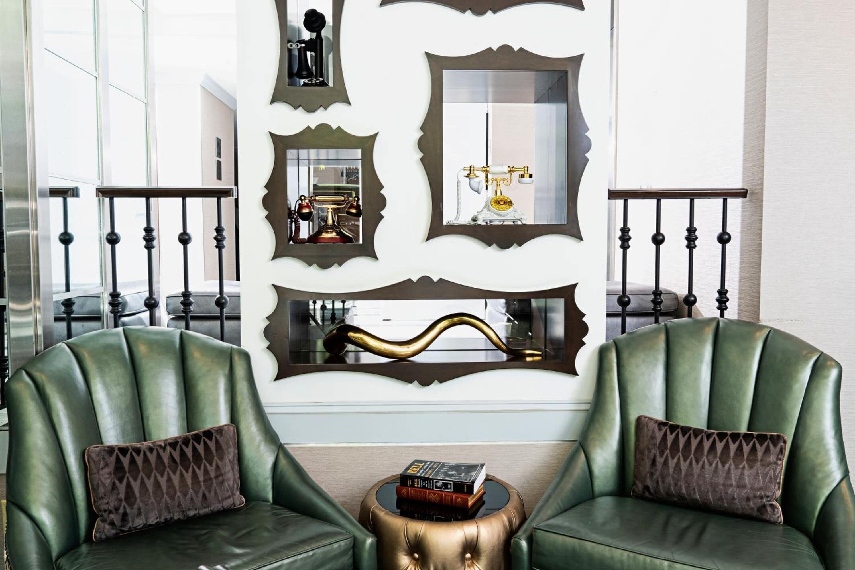 Una habitación con dos sillones de cuero verde, una mesita redonda con libros y espejos decorativos en la pared.