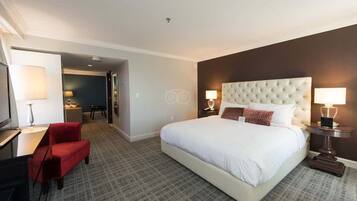 A hotel room with a large bed, a red chair, a desk, and a TV.