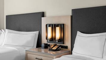 A hotel room with two beds, a bedside table with a lamp, a telephone, and a small drawer.