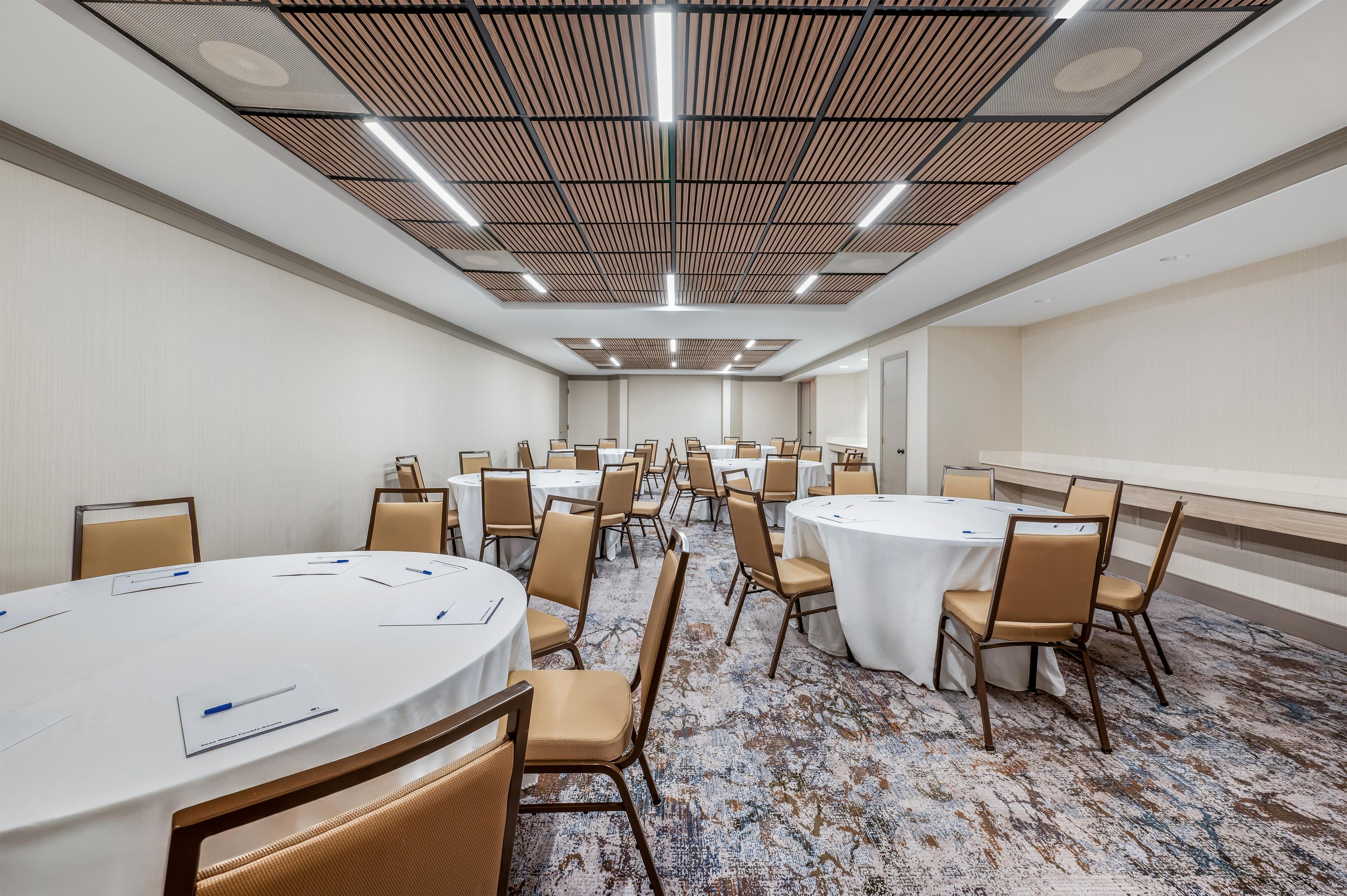 A conference room with multiple round tables and chairs, a patterned carpet, and a ceiling with a grid-like design.