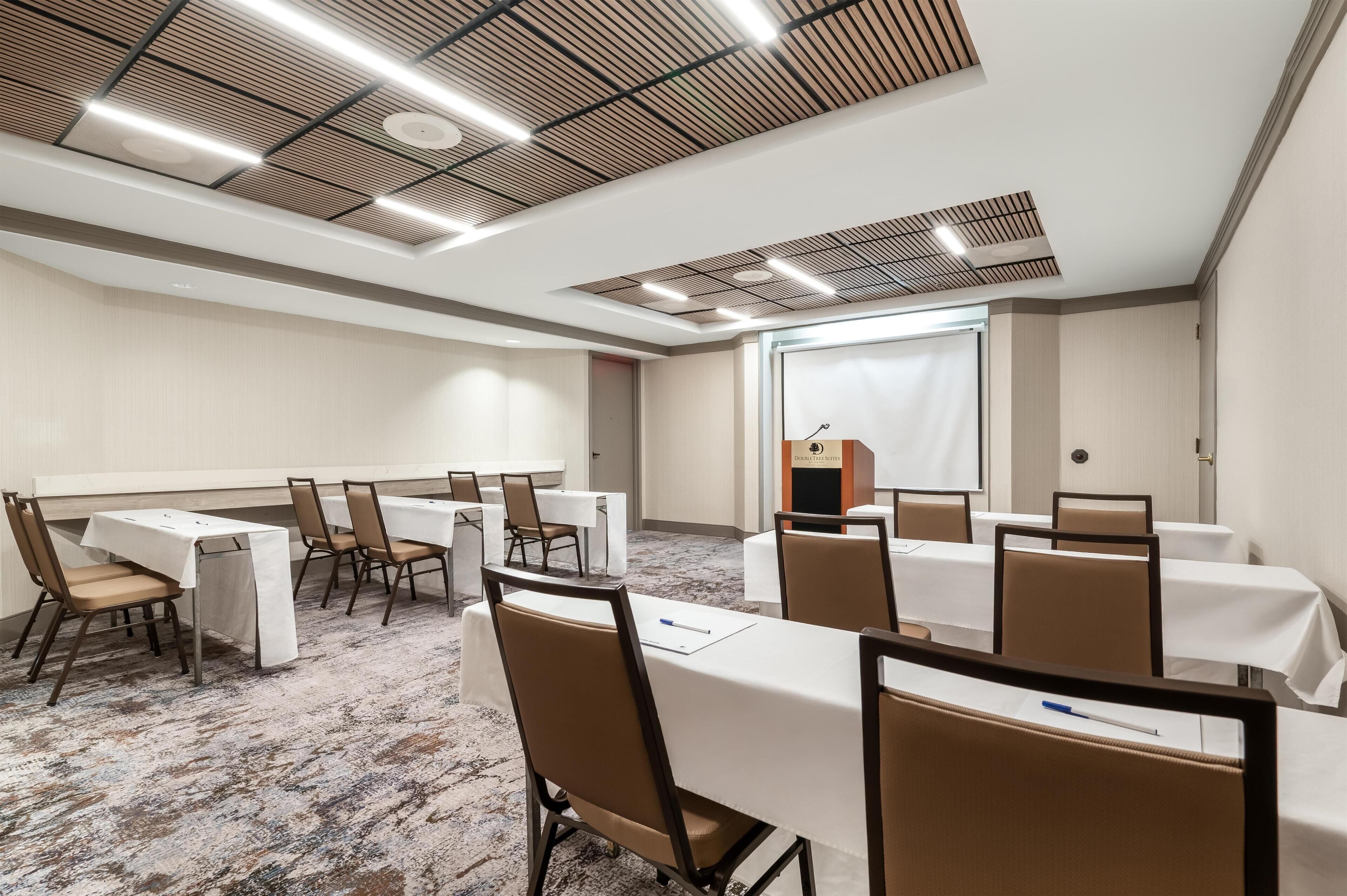 Un salón de conferencias con mesas, sillas, un atril y un ventanal grande.