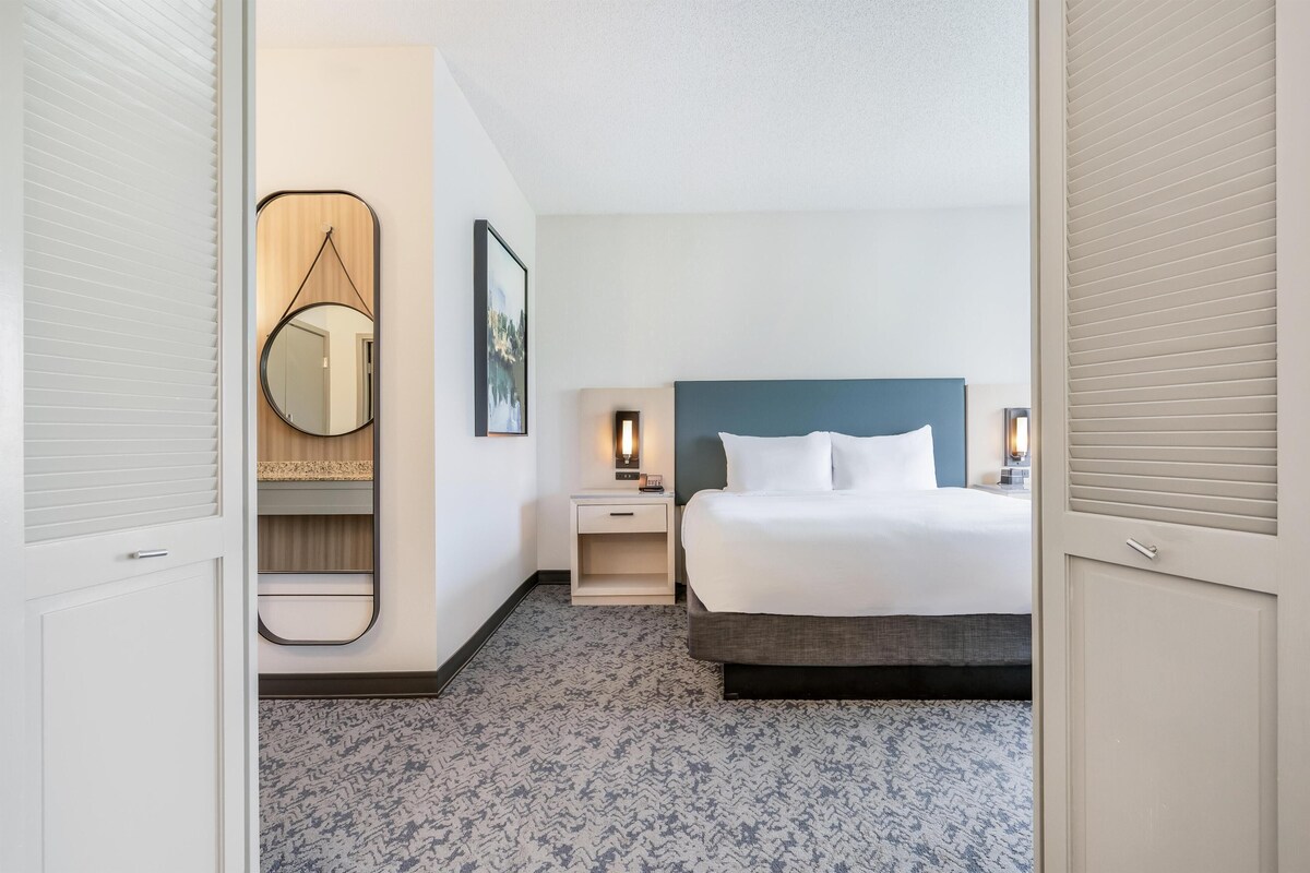 A hotel room with a bed, bedside tables, a mirror, and a framed picture on the wall.
