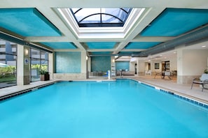 Una amplia piscina cubierta con tragaluces arriba, rodeada de zonas de descanso y vistas al exterior.
