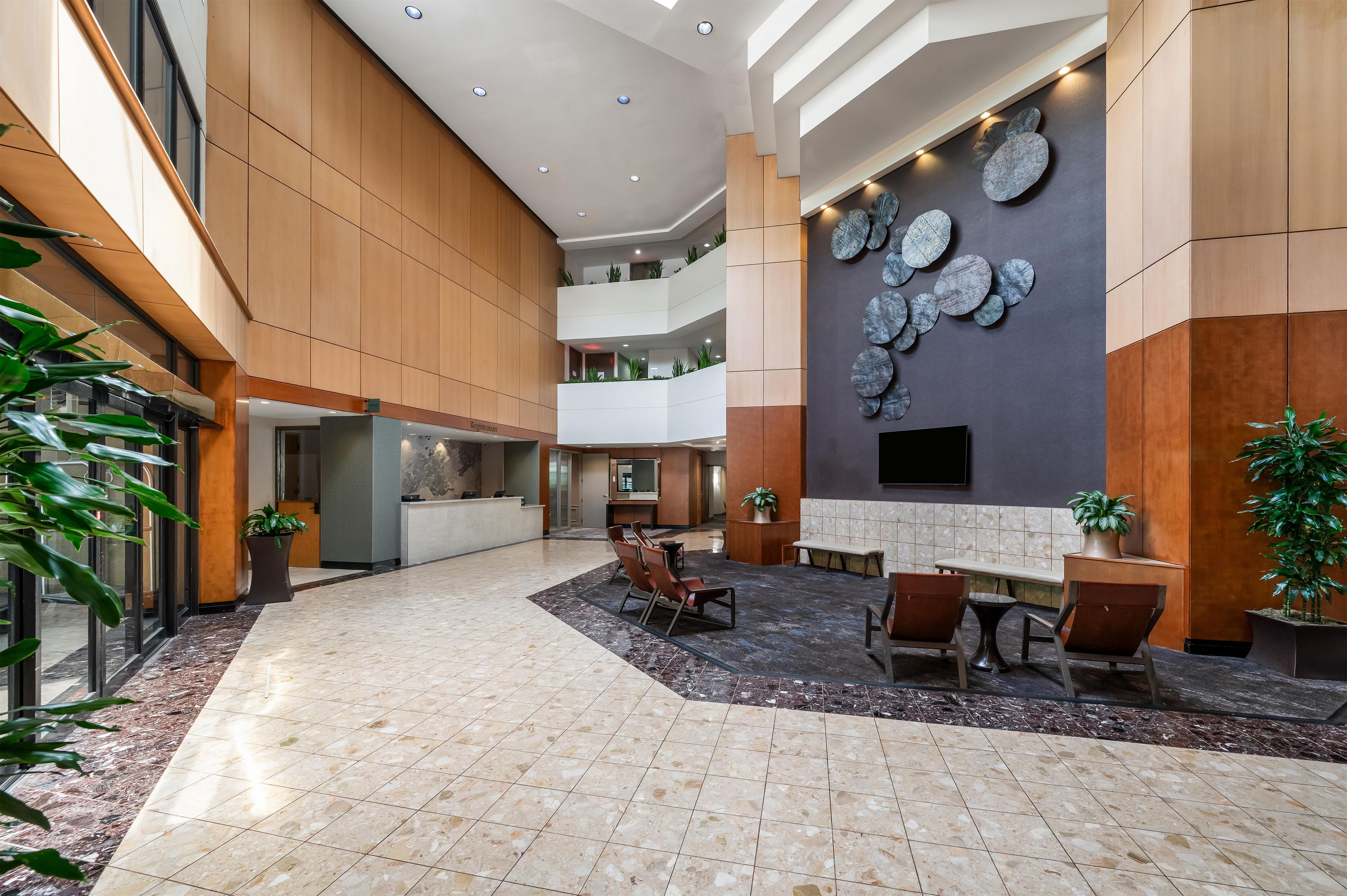 A spacious lobby with a high ceiling, a reception desk, seating area, and a wall-mounted decorative element.