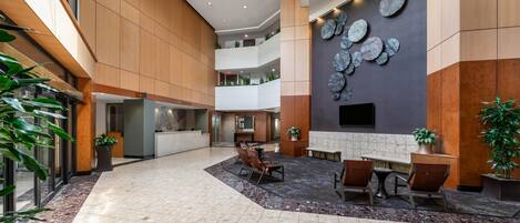 A spacious lobby with a high ceiling, a reception desk, seating area, and a wall-mounted decorative element.