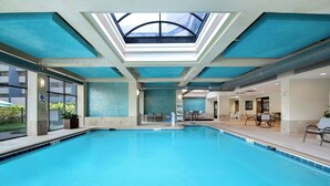 Une grande piscine intérieure dotée d’un toit en verre, de murs en verre transparent et d’un sol carrelé.