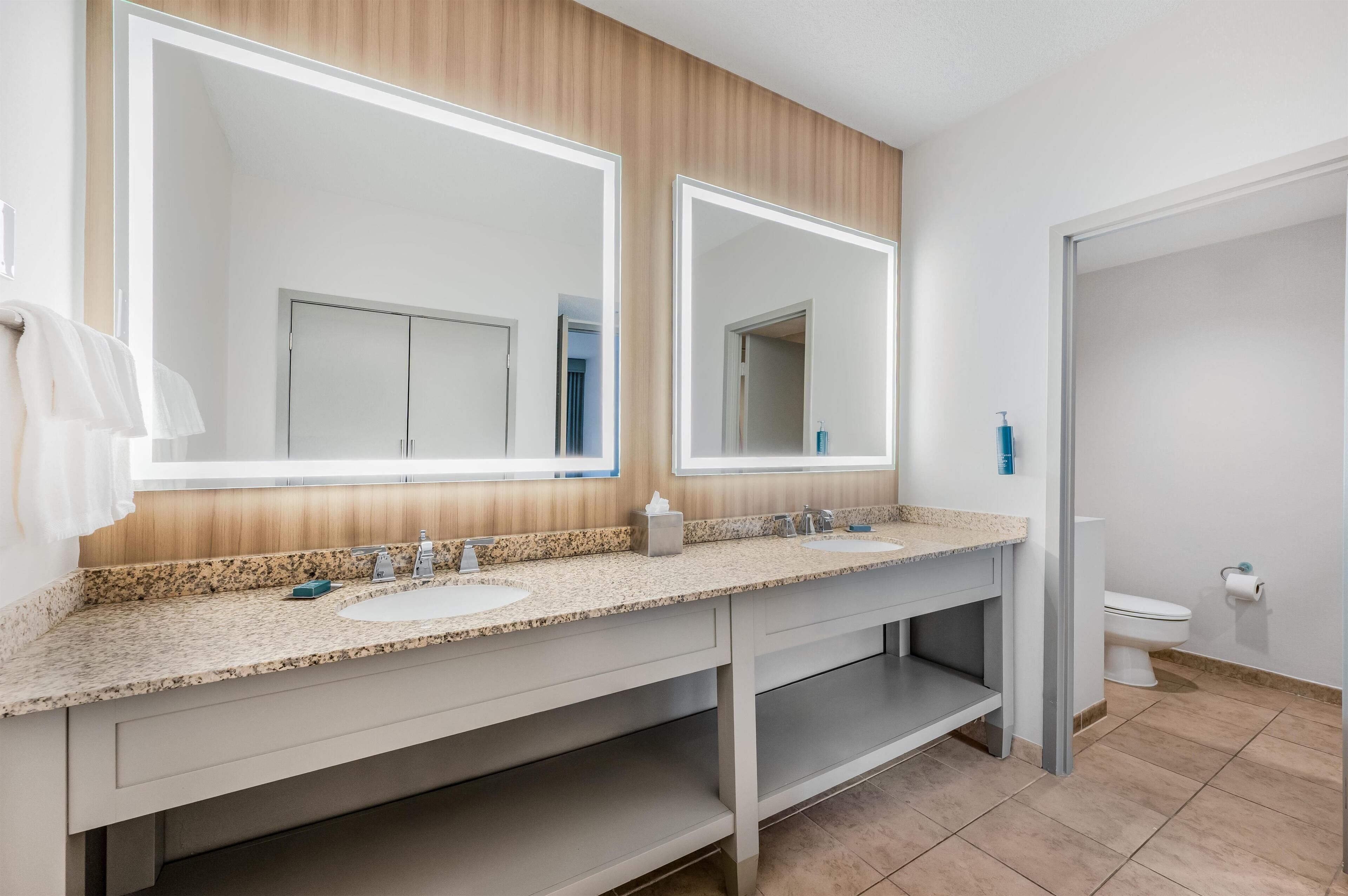 A modern bathroom with two sinks, a large mirror, and a toilet.