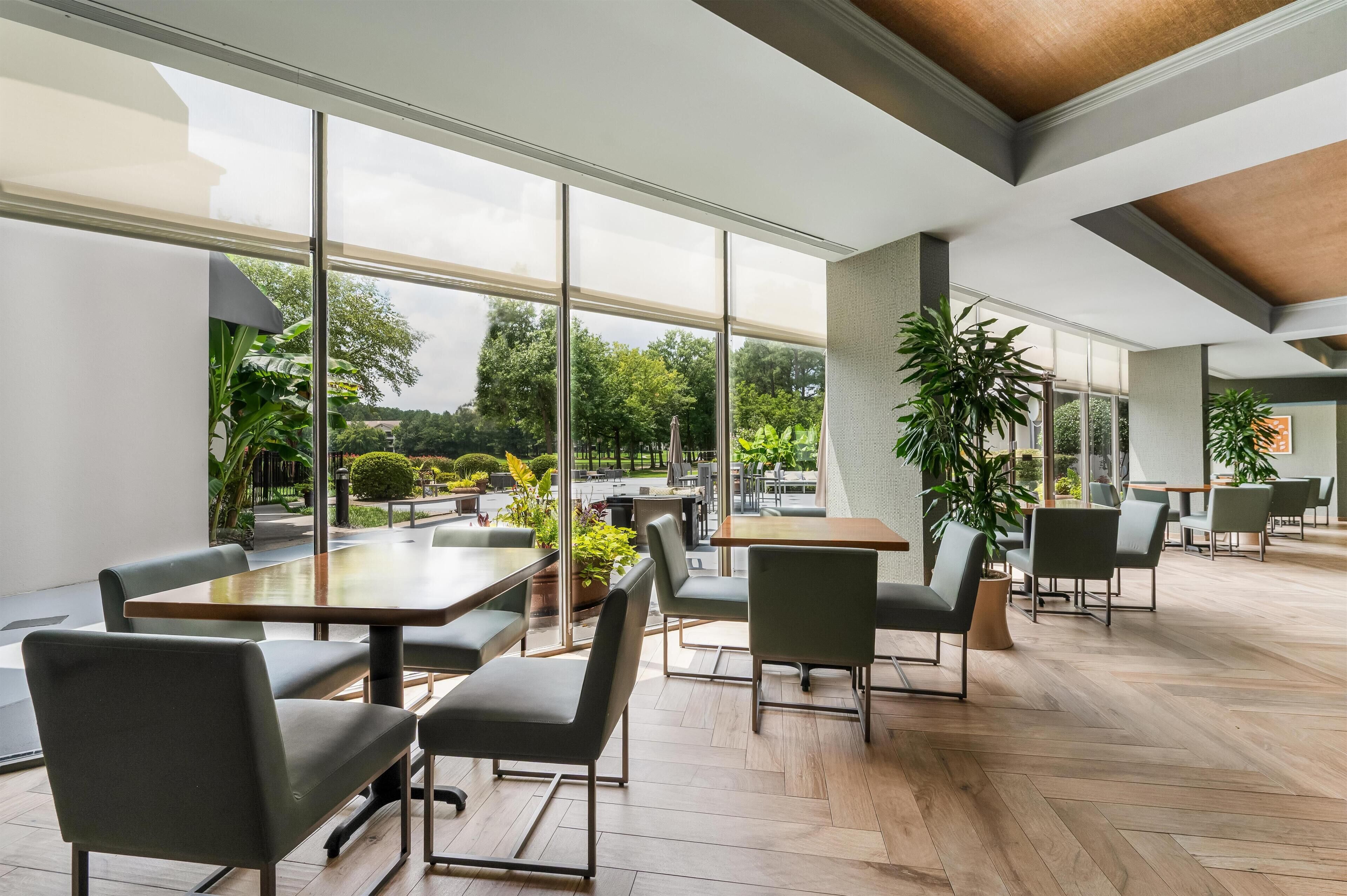 A spacious indoor area with large windows, wooden flooring, and modern furniture.