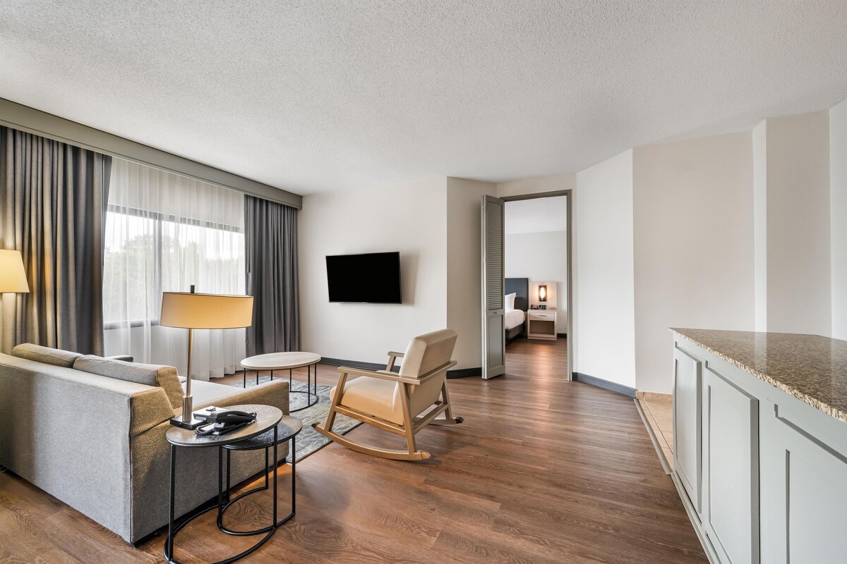 Une chambre d’hôtel équipée d’un canapé, d’un fauteuil, d’une petite table, d’une télévision et d’un coin cuisine.