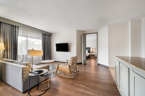 A hotel room with a sofa, a chair, a small table, a TV, and a kitchen area. - DoubleTree Suites by Hilton Raleigh - Durham (Durham)