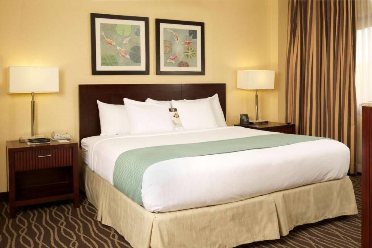 A hotel room with a large bed, two bedside tables with lamps, a headboard, and two framed wall art pieces.