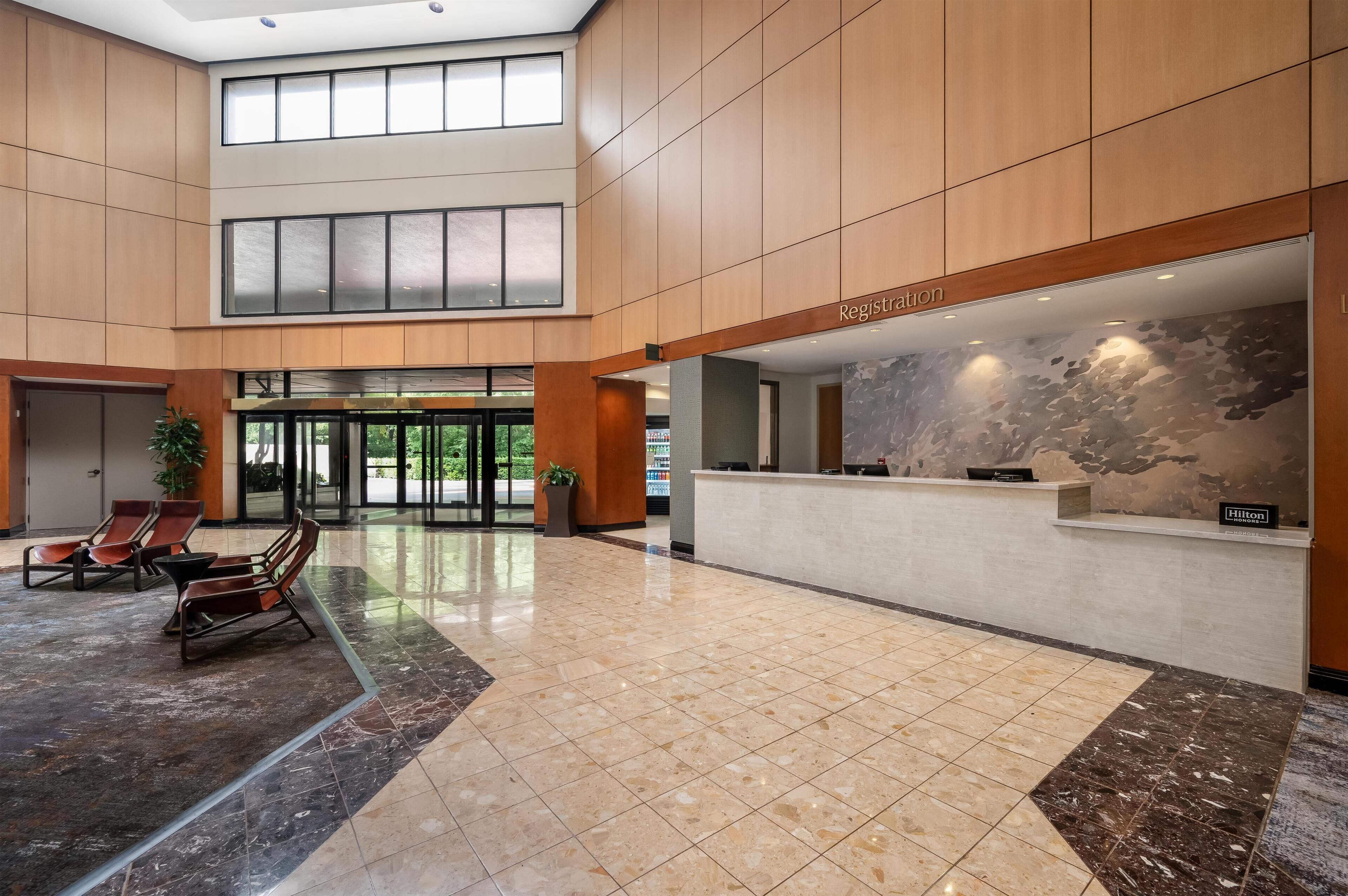 A hotel lobby with a reception desk, seating area, and a large glass door entrance.