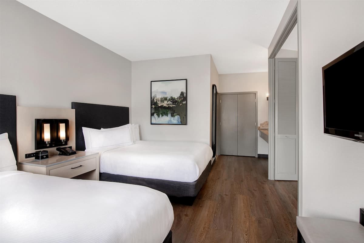 A hotel room with two beds, a desk with a telephone, a flat-screen TV, and a painting on the wall.