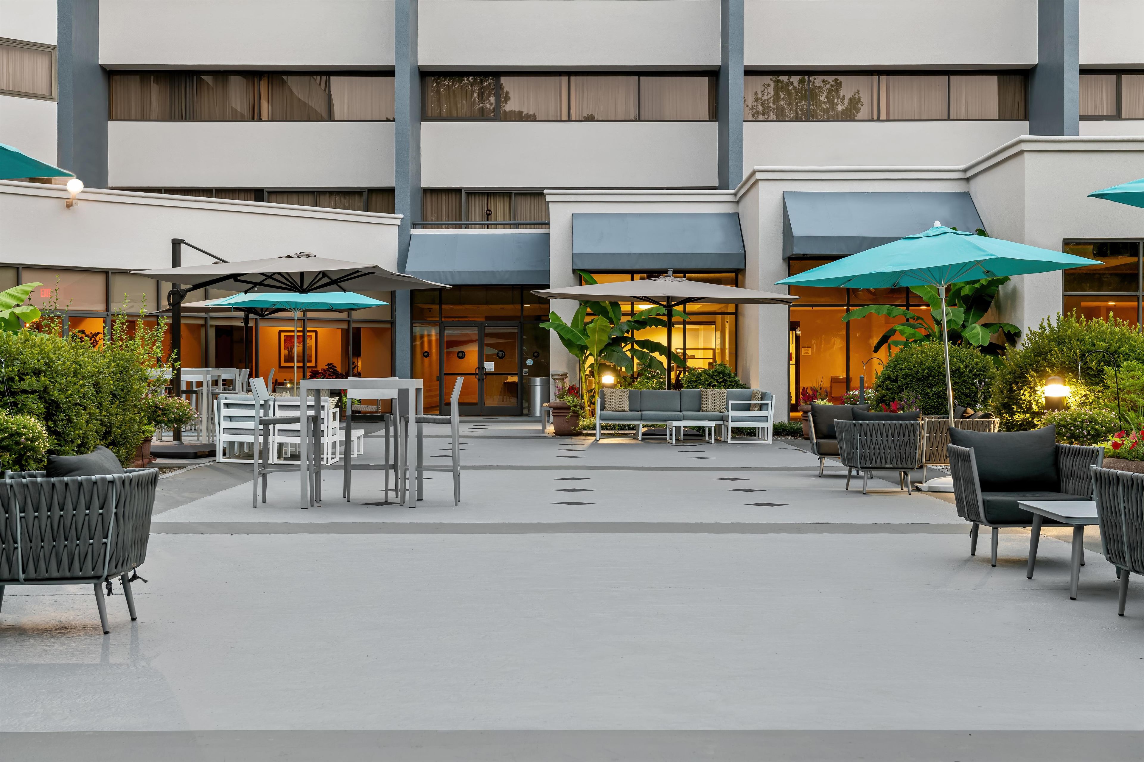 An outdoor seating area with tables and chairs, umbrellas, and potted plants.