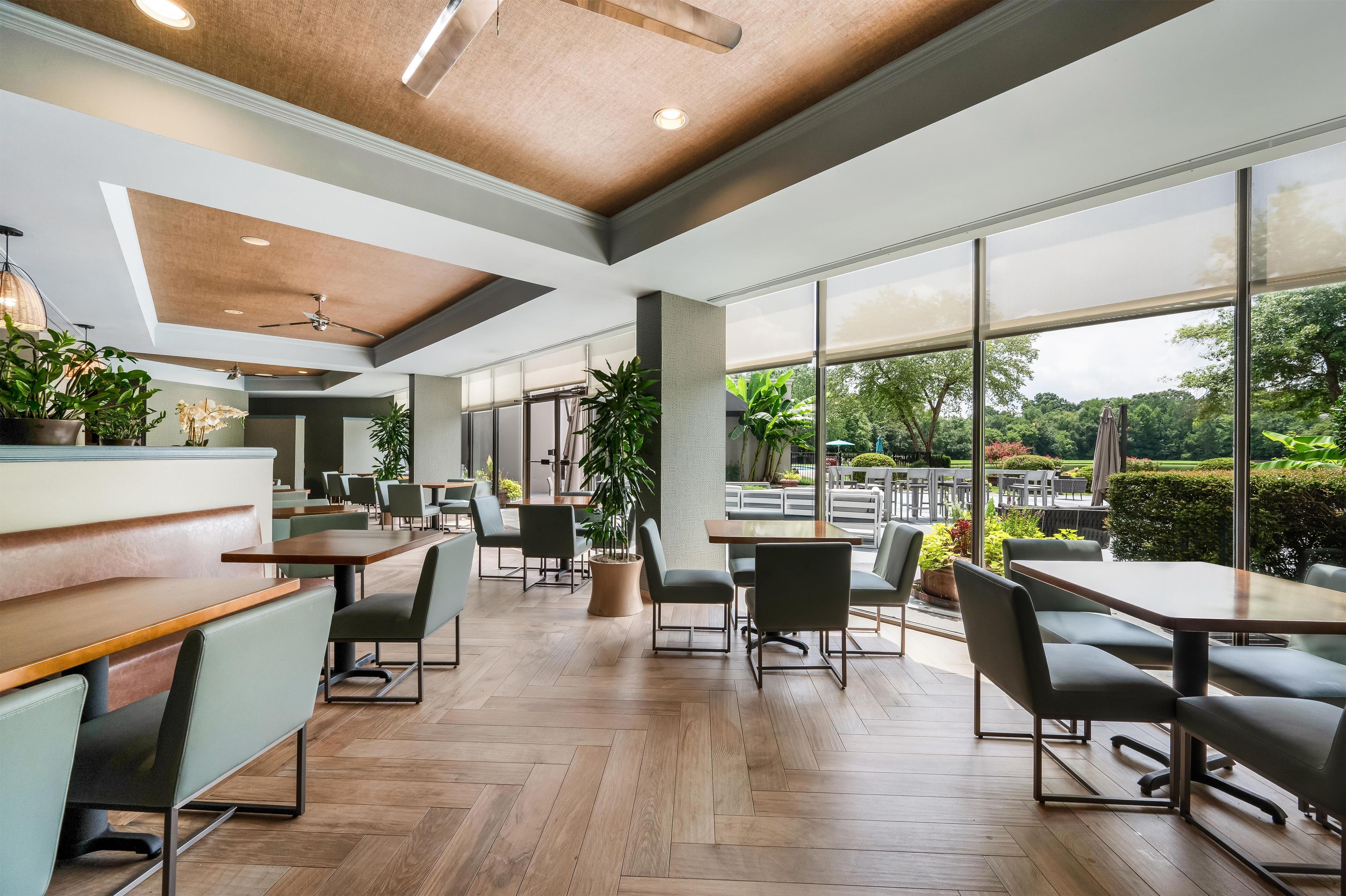 A spacious indoor area with wooden flooring, multiple seating arrangements, and large windows offering a view of the outdoors.