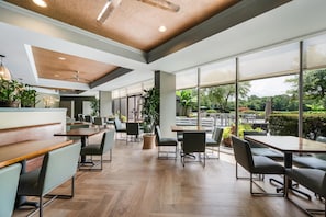 A spacious indoor area with wooden flooring, multiple seating arrangements, and large windows offering a view of the outdoors. - DoubleTree Suites by Hilton Raleigh - Durham (Durham)
