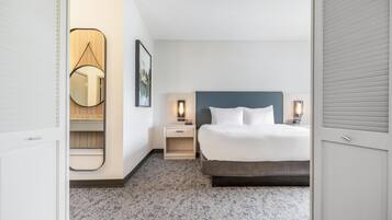 Una habitación de hotel con una cama, mesitas de noche, un espejo y un cuadro en la pared.