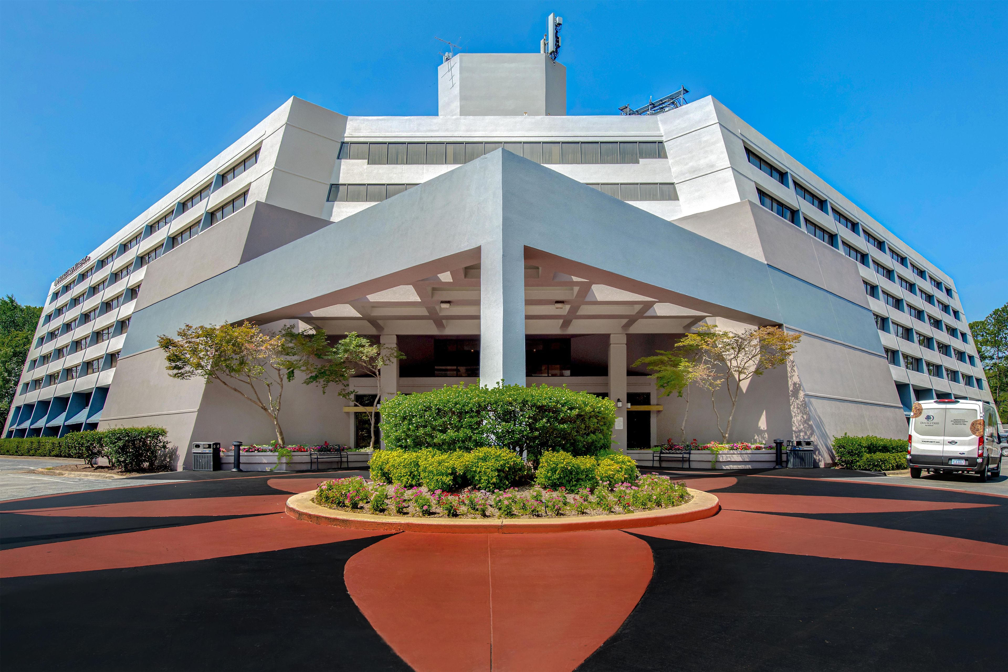 A modern hotel with a distinctive geometric entrance, a landscaped garden, and a clear blue sky.