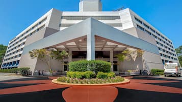 A modern hotel with a distinctive geometric entrance, a landscaped garden, and a clear blue sky.